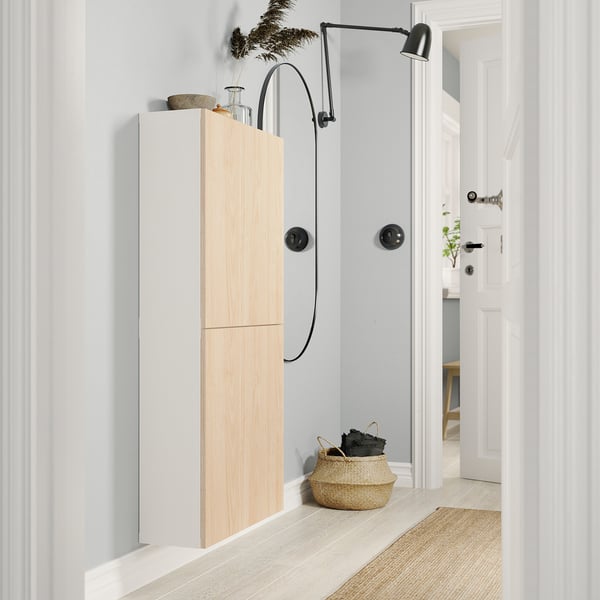 Moderne hal met witte BESTÅ opbergkast, natuurlijke houten deuren, zwarte wandlamp, rieten mand, lichte houten vloeren.