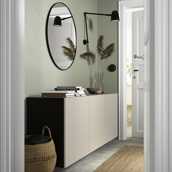 Wit BESTÅ dressoir met spiegel, boeken, vazen, planten; Groene muur, zwarte lampen, gevlochten mand.