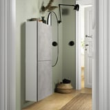 Smalle BESTÅ unit met 2 deuren op groene muur, witte deuren, zwarte lamp, mand met handdoeken.