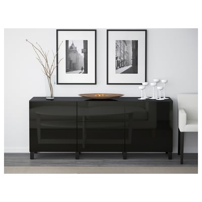 Modern zwart glazen dressoir met lades en legplanken. Bekroond met decoratieve schaal en vazen, tegen een witte muur met ingelijste foto's.