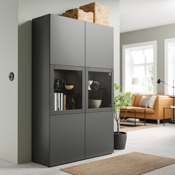 Moderne woonkamer met BESTÅ glazen opbergruimte, mand, plant, beige vloerkleed.
