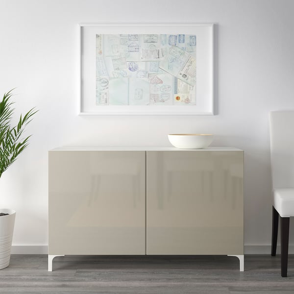 Minimalistische woonkamer met een BESTÅ dressoir met reflecterend oppervlak en een witte schaal, vergezeld van een ingelijste collageprint.