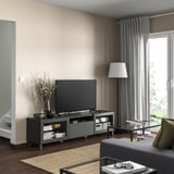 Moderne woonkamer met BESTÅ tv-meubel in zwart, voorzien van een flatscreen-tv, witte lamp, grijze gordijnen, houten vloer en een vloerkleed.