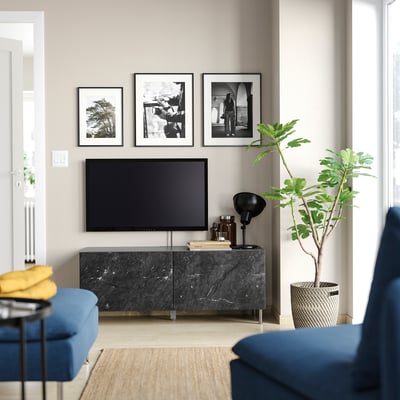 Moderne woonkamer: blauwe bank, zwarte tv op donkere marmeren kast, drie zwart-witte frames, grote groene plant, gele plaid.