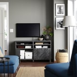 Moderne woonkamer met zwart BESTÅ tv-meubel, marmeren blad, bloemen, boeken, foto's, blauwe bank en mand.