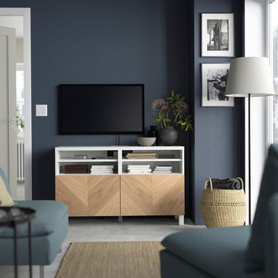 Wit BESTÅ tv-meubel, flatscreen tv, blauwe stoelen, mand, lamp, donkere muren, foto's, bank, vloerkleed.