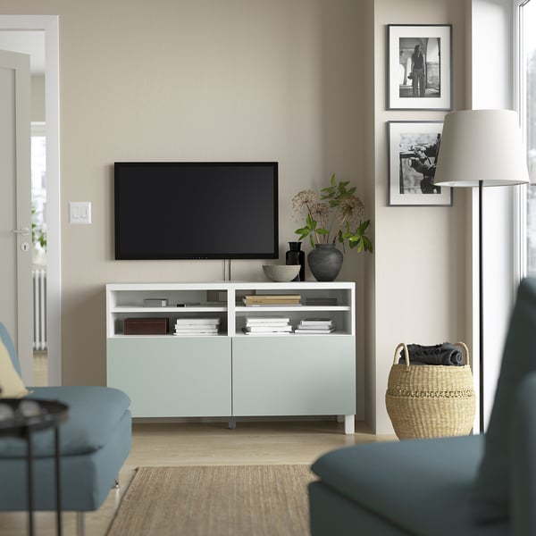 Moderne woonkamer met BESTÅ tv-meubel in lichtblauw, flatscreen-tv, blauwe bank, mand, lamp en zwart-witfoto's.