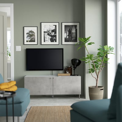 Moderne woonkamer met grijs BESTÅ tv-meubel, flatscreen-tv, blauwe bank, zwart-witportretten en groene plant.