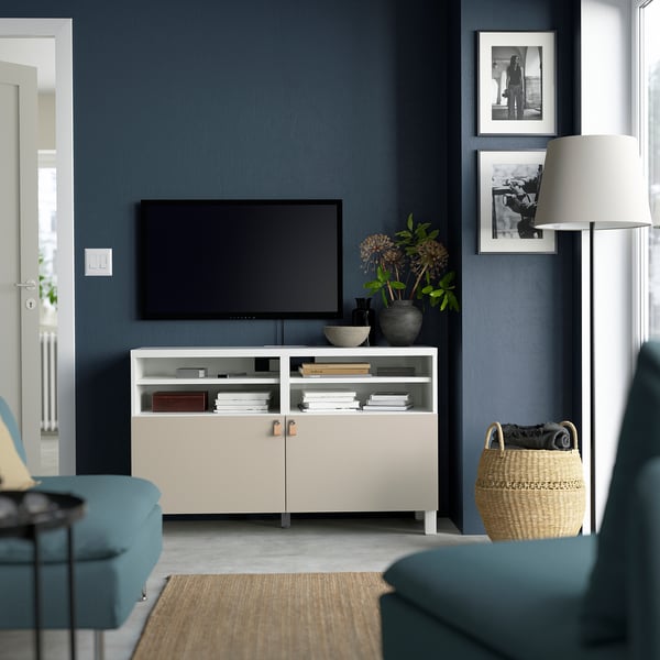 Moderne woonkamer met BESTÅ tv-meubel, flatscreen, bloemen, foto's, mand, lamp. Muur is donkerblauw.