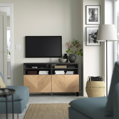 Moderne woonkamer met BESTÅ tv-meubel, tv, boeken, vazen en kunst. Blauwe banken, vloerlamp en mand in de buurt.