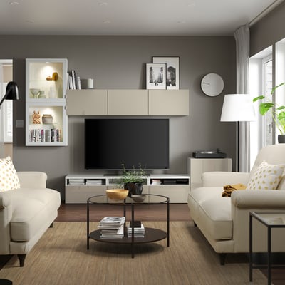 Moderne woonkamer met licht meubilair, grote tv, banken, salontafel en planten.