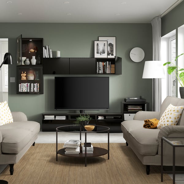 Moderne woonkamer met groene muren, tv en boekenplanken. Salontafel, banken, lamp en klok maken het decor compleet.