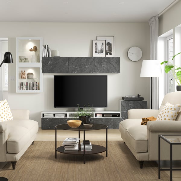 Moderne woonkamer met BESTÅ tv-meubel, lichtbeige banken, zwarte salontafel, grote flatscreen-tv, witte hanglamp en groene plant.