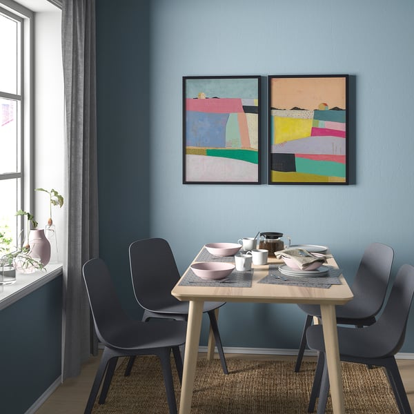 Moderne eetkamer met abstracte kunst, houten tafel, grijze stoelen, roze kommen, witte mokken, zwarte theepot en een groot raam.