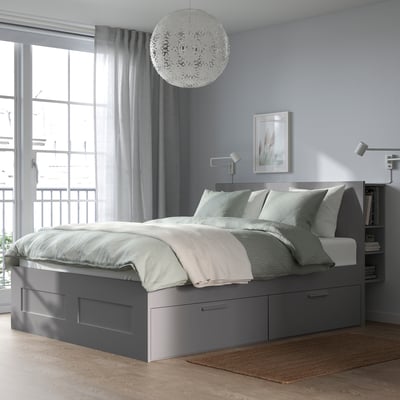 Modern grijs BRIMNES bed met opbergruimte, blauwe muur, hanglamp, raam met gordijnen, grijs vloerkleed, houten vloer.