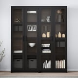 Een BRIMNES zwarte vitrinekast met glazen deuren, met boeken en decor.