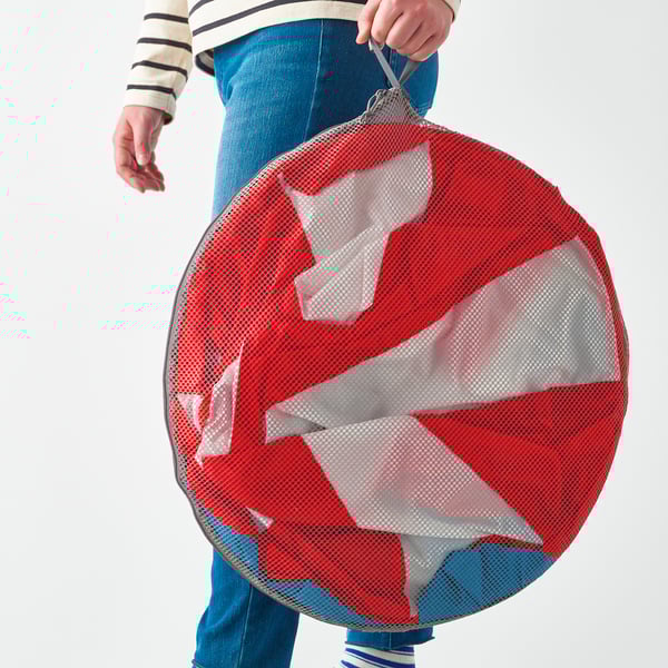 Persoon die een grote rode gaascirkel met witte stof aan de binnenkant houdt, waarschijnlijk een kinderspeeltent.