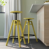 Twee felgele DALFRED krukken in moderne keuken, in hoogte verstelbaar, driepoot design.
