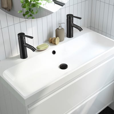 Moderne wastafel in de badkamer met strakke zwarte kraan en hendel voor waterefficiëntie, geflankeerd door zeepdispenser en accessoires op wit aanrechtblad.