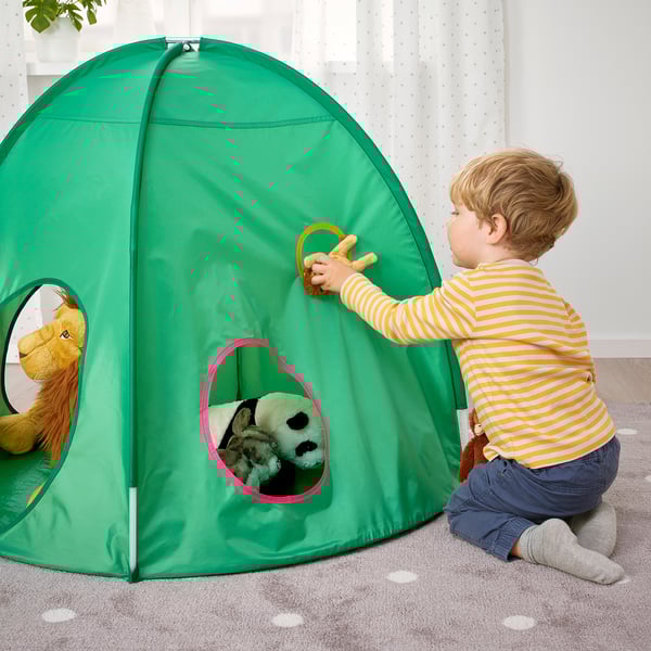 Het spelen van het kind met groene pop-up tent. De jongen in gestreept overhemd opent tentflap en onthult opgezette dieren binnenin.