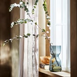 Moderne woonkamer met houten plank, blauwe zandlopervaas van eucalyptus, boeken, kom en vitrages.