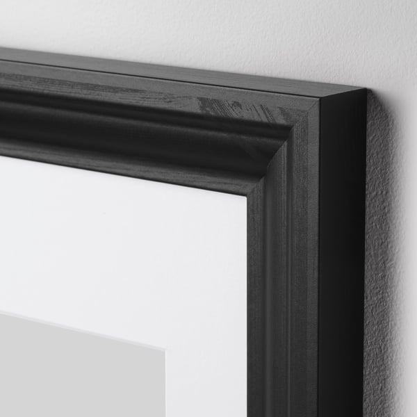 Zwarte houten fotolijst met stevige, gladde randen en heldere, witte binnenkant, gemonteerd op een witte muur.