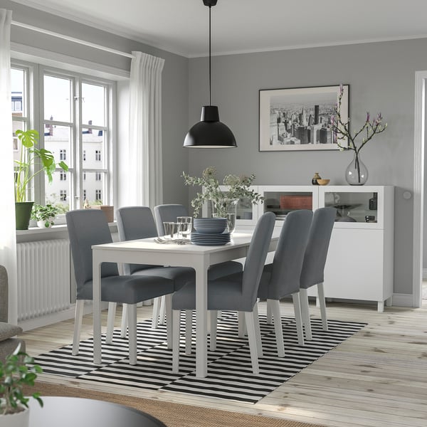 Moderne eethoek met witte uitschuifbare tafel, grijze stoelen, zwarte hanglamp, gestreept vloerkleed en planten.