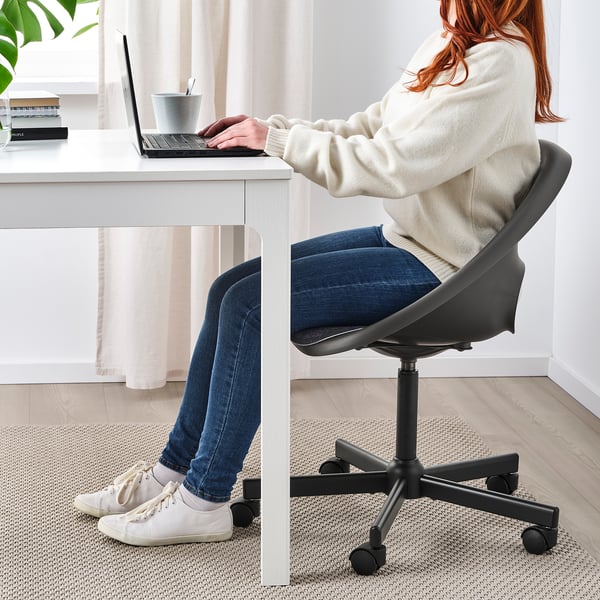 Persoon gebruikt laptop in ELDBERGET stoel met gordijnen & plant.