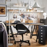 Modern kantoor aan huis met twee zwarte ELDBERGET bureaustoelen, houten tafel, ophangbord en planken vol met decor en benodigdheden.