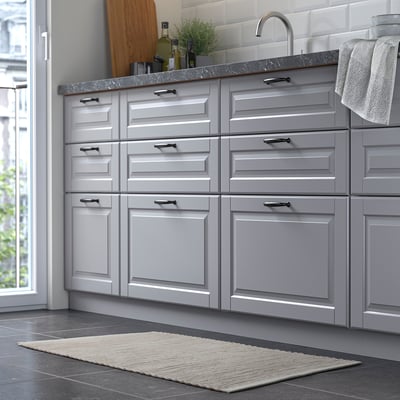 Moderne keuken met grijze kasten, gootsteen en een klein, handgeweven, beige vloerkleed op de donkere vloer.