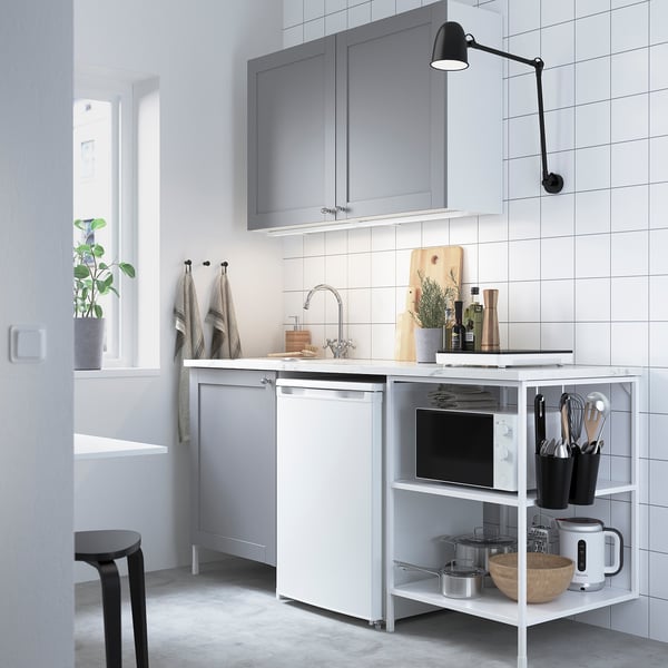 Moderne grijze keuken met wit aanrecht, roestvrijstalen spoelbak, zwart gereedschap, planten en wandlamp. Grijze kasten, open planken met magnetron en waterkoker.