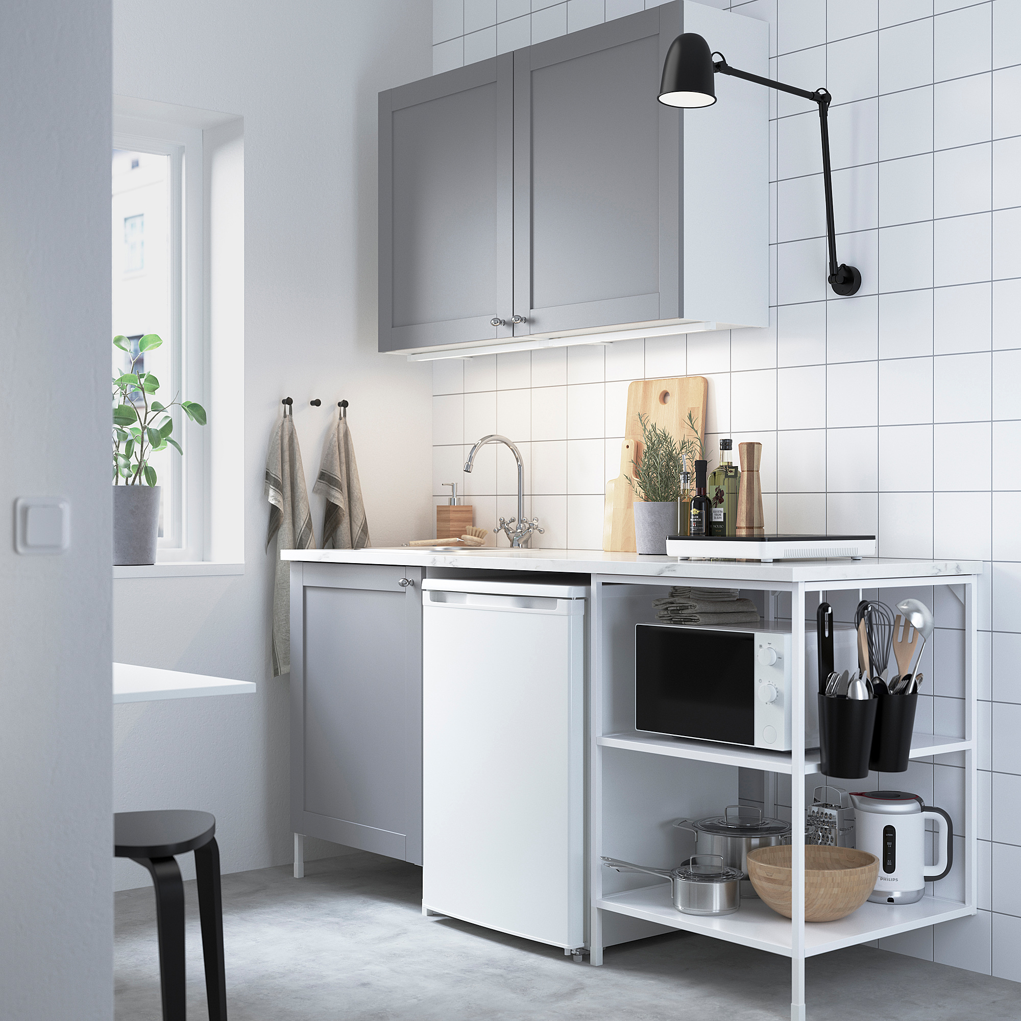 Moderne grijze keuken met wit aanrecht, roestvrijstalen spoelbak, zwart gereedschap, planten en wandlamp. Grijze kasten, open planken met magnetron en waterkoker.