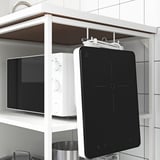 Zwarte tablet hangt aan haken van de plank, naast een witte magnetron.