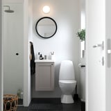 Moderne badkamer met grijze ENHET onderkast, strak wit toilet en ronde spiegel. Compact en toch stijlvol, geschikt voor kleine ruimtes.
