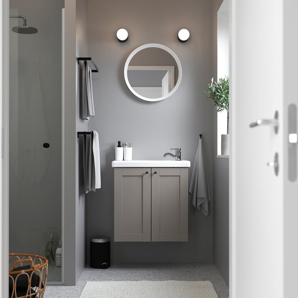 Moderne badkamer met ENHET grijze wastafelmeubel, ronde spiegel, strakke wastafel, handdoeken en planten. Compact ontwerp, zwevende kast voor kleine ruimtes.