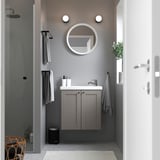 Moderne badkamer met ENHET grijze wastafelmeubel, ronde spiegel, strakke wastafel, handdoeken en planten. Compact ontwerp, zwevende kast voor kleine ruimtes.