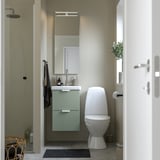 Moderne badkamer met ENHET saliegroen 2-ladekast, strak wit toilet, glazen douche en wandspiegel. Compact ontwerp maximaliseert de ruimte.