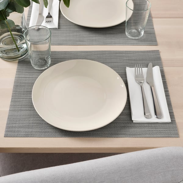 Tafel set met wit servies op grijze placemats, inclusief borden, glazen en bestek.