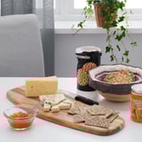 Houten snijplank met kaas, crackers, mes en jam op eettafel, gebruikt voor het serveren van voedsel.