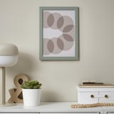 Aan een muur hangt een groen ingelijste foto, omgeven door een wit bureau met decoratieve voorwerpen zoals een lamp, een plant en houten kralen.