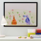 Childs tekening in zwart frame op wit bureau. Linker lamp verlicht kunstwerken en schoolbenodigdheden.