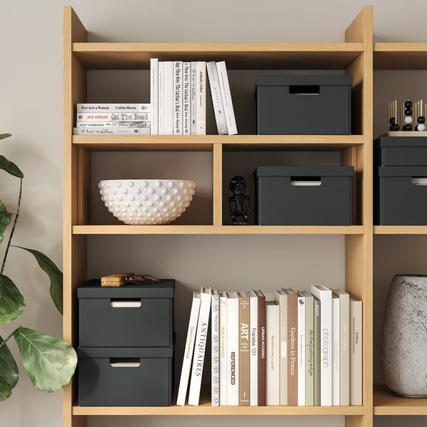 Houten boekenkast met boeken, decoratieve schaal en opbergdozen.