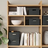 Houten boekenkast met boeken, decoratieve schaal en opbergdozen.