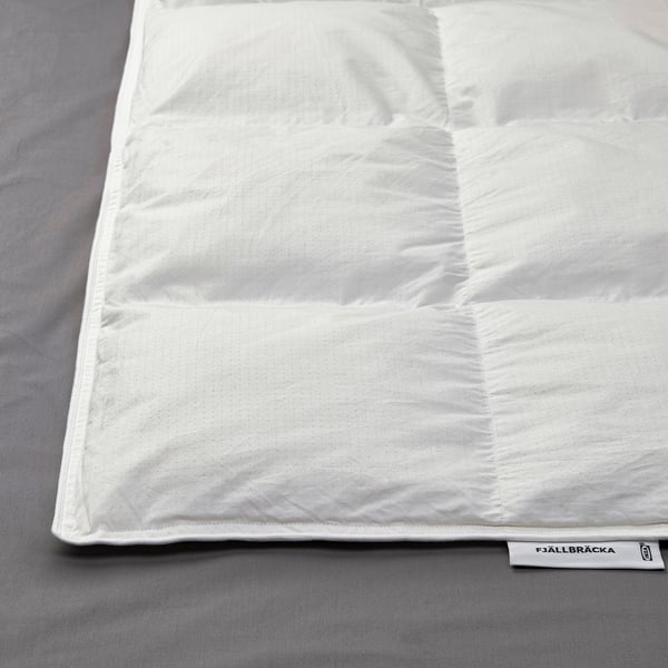 Schoon wit dekbed netjes opgevouwen op grijs beddengoed. Op het label staat FJÄLLBRÄCKA met vulling van gerecycled dons.