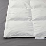 Schoon wit dekbed netjes opgevouwen op grijs beddengoed. Op het label staat FJÄLLBRÄCKA met vulling van gerecycled dons.