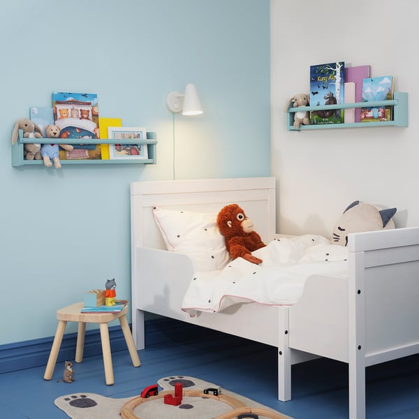 Blauwe kinderkamer met wit bed, FLISAT-opslag , boeken, speelgoed, vloerkleed en treinspoor.