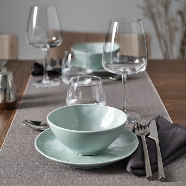 Turquoise-grijze porseleinen kom en bord met wijnglazen en bestek op een tafel.