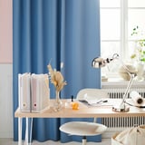 Modern kantoor aan huis met blauwe gordijnen, houten bureau, witte stoel en verstelbare zilveren FORSÅ lamp.