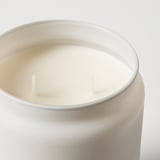 Close-up van een ronde geurkaars in een matglazen pot met twee lonten.