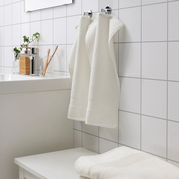 Witte FREDRIKSJÖN handdoeken hangen netjes aan het wandrek, naast tandenborstels en plant.